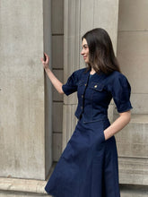 A lady wears a denim top and a blue skirt.